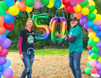 Zentrumsleitung des Kinder- und Familienzentrums Flintacker steht in einem bunten Luftballonbogen und hält eine bunte Ballon-50